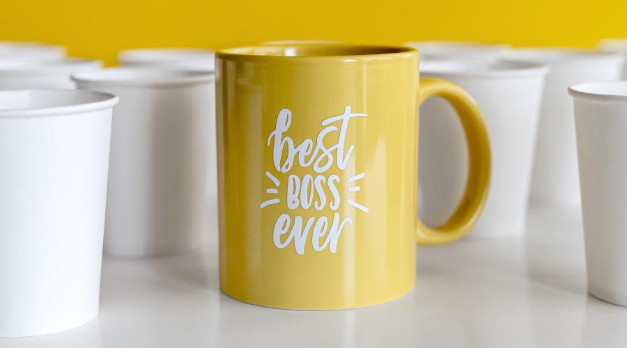 A yellow mug that says "Best Boss" sits among white paper coffee cups. 