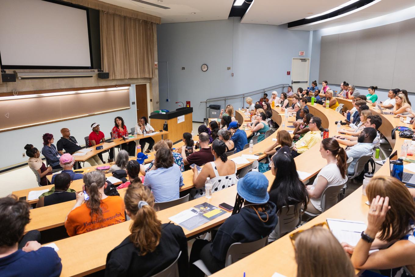 large audience listens to diverse panelists at the front of the room