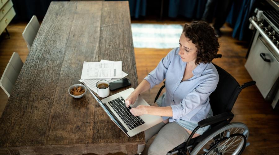 Photo of woman in a wheelchair at a table with laptop and letters beside her.