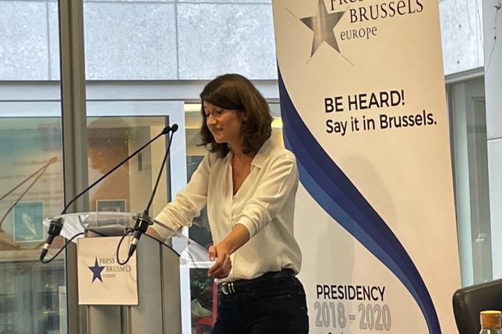 MEP Lara Wolters stands at a lecturn with a Press Club Bussels Europe sign on it, in front of a white banner with black and blue text that says "Press Club Brussels Europe" and "Be Hear. Say it in Brussels" at an event