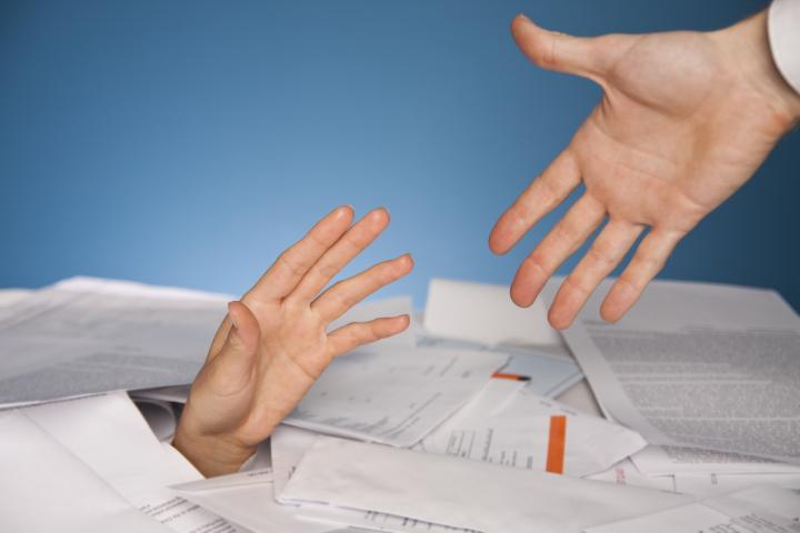 Outstretched hand reaches out from a pile of papers to another hand